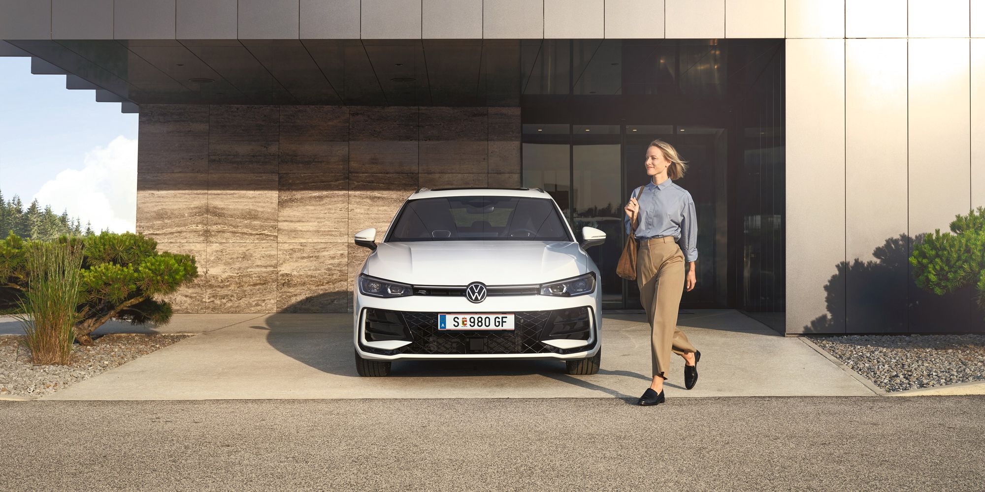 Frontansicht eines weißen VW Passat R-Line, eine Frau geht an ihm vorbei.