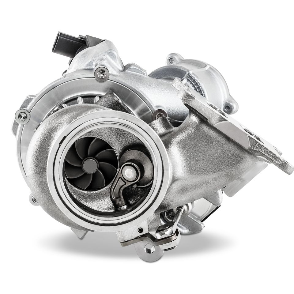 Ein metallischer Turbolader für einen Verbrennungsmotor, freigestellt vor weißem Hintergrund. Deutlich sichtbar sind das Gehäuse, das Verdichterrad mit seinen Schaufeln und der Abgasanschluss.