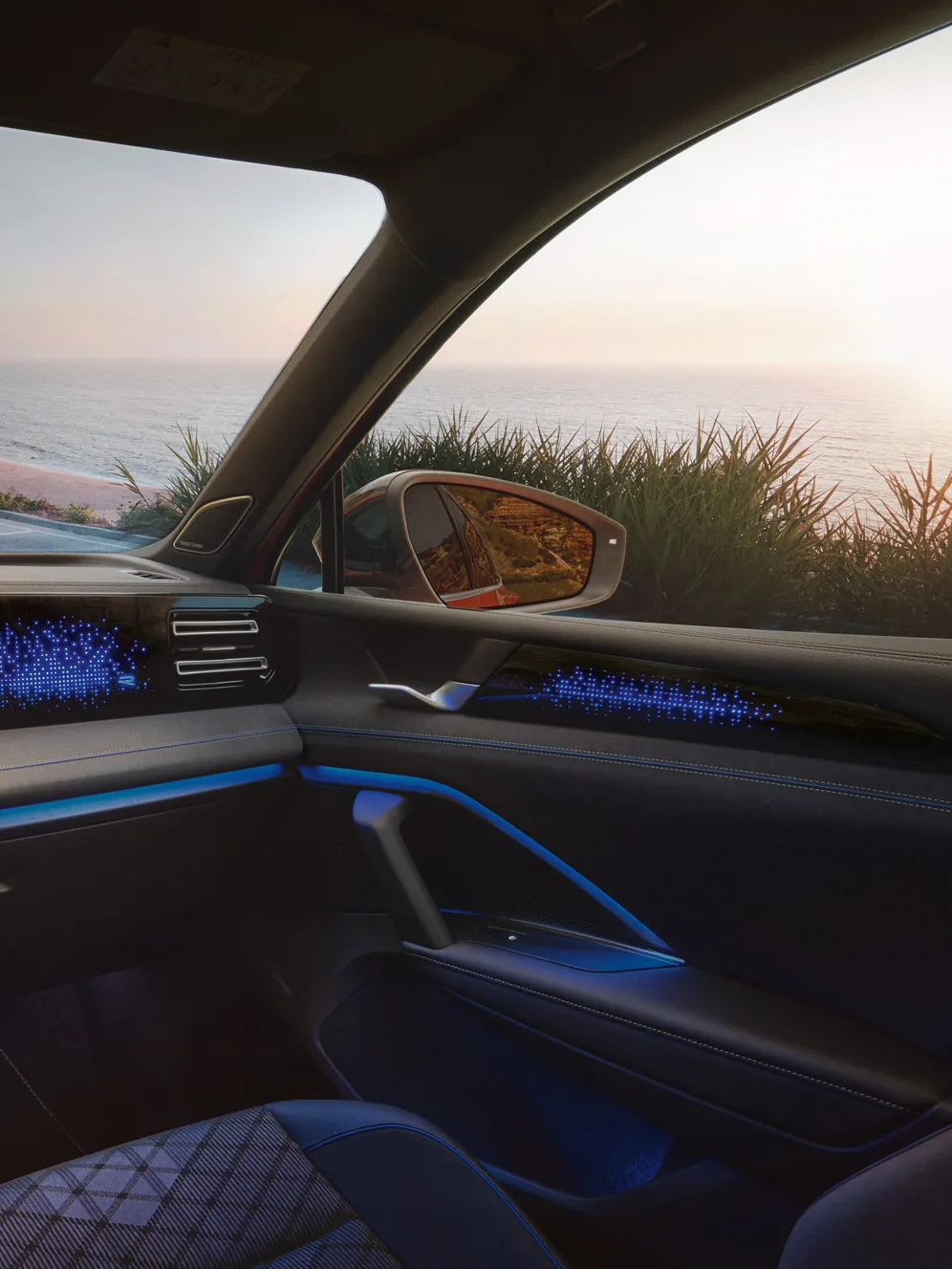 VW Tiguan mit blauer Ambientebeleuchtung. Durch die Frontscheibe ist ein Küstenlandschaft und ein auf das Meer schauendes Paar sichtbar.
