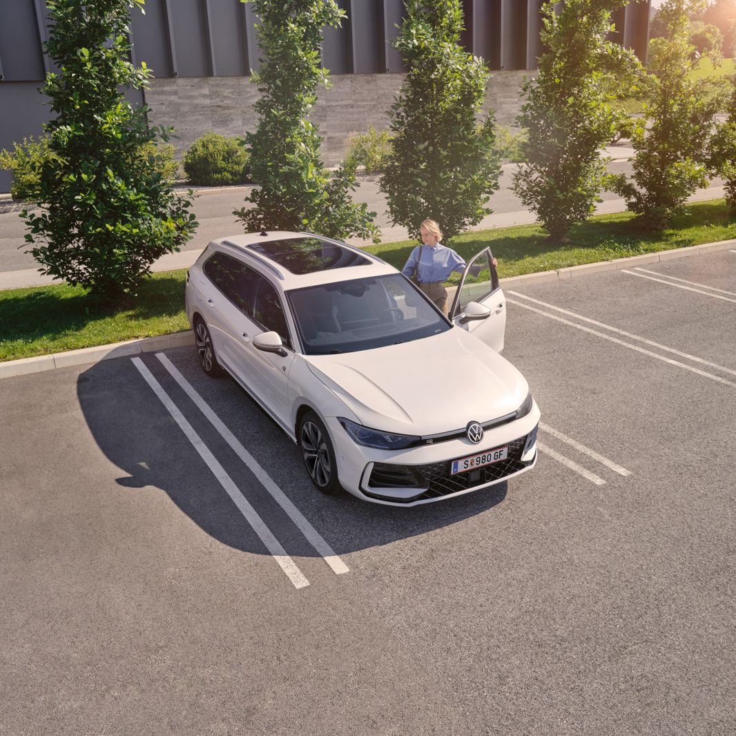 Weißer VW Passat parkt vor einem modernen Bürogebäude. Eine Frau steigt ein.