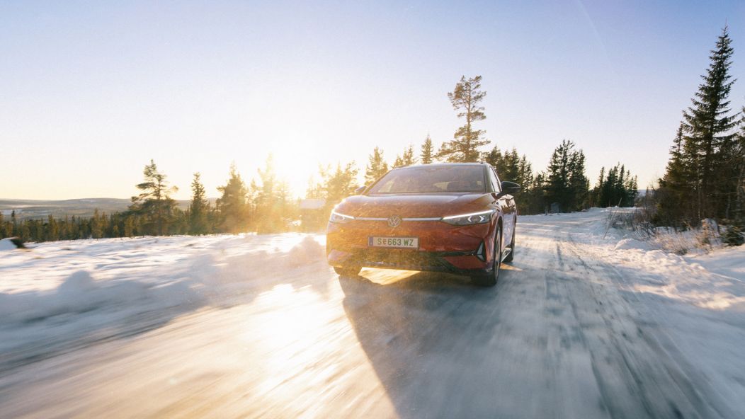 Ein roter ID.7 fährt auf einer eisigen Straße bei Sonnenaufgang. Im Hintergrund sind verschneite Wälder und Berge zu sehen. Die Sonne scheint hell und wirft lange Schatten.