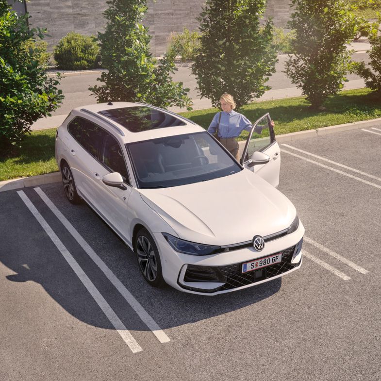 Weißer VW Passat parkt vor einem modernen Bürogebäude. Eine Frau steigt ein.