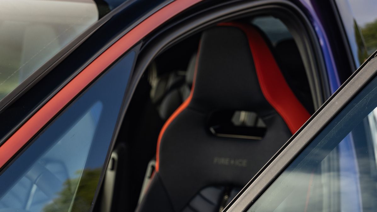 Nahaufnahme eines geparkten Autos in blauer Farbe mit roten Akzenten. Auf der Tür steht "GTX | FIRE+ICE" und im Hintergrund ist ein schwarzer Sitz mit roter Umrahmung. Die Autotür und der Seitenspiegel sind ebenfalls sichtbar.