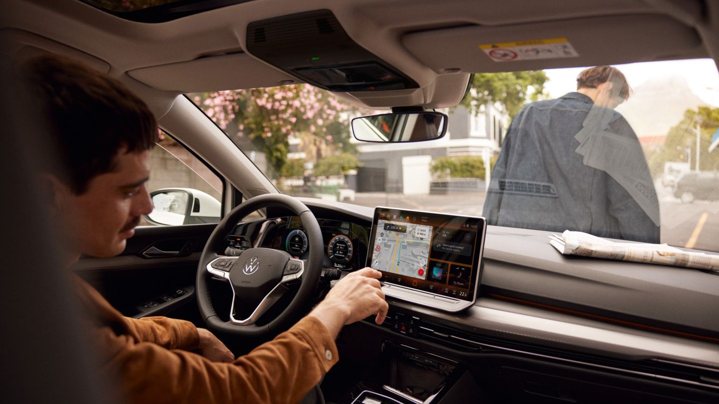 Ein Mann sitzt im parkenden VW Golf und bedient das Navigationssystem.