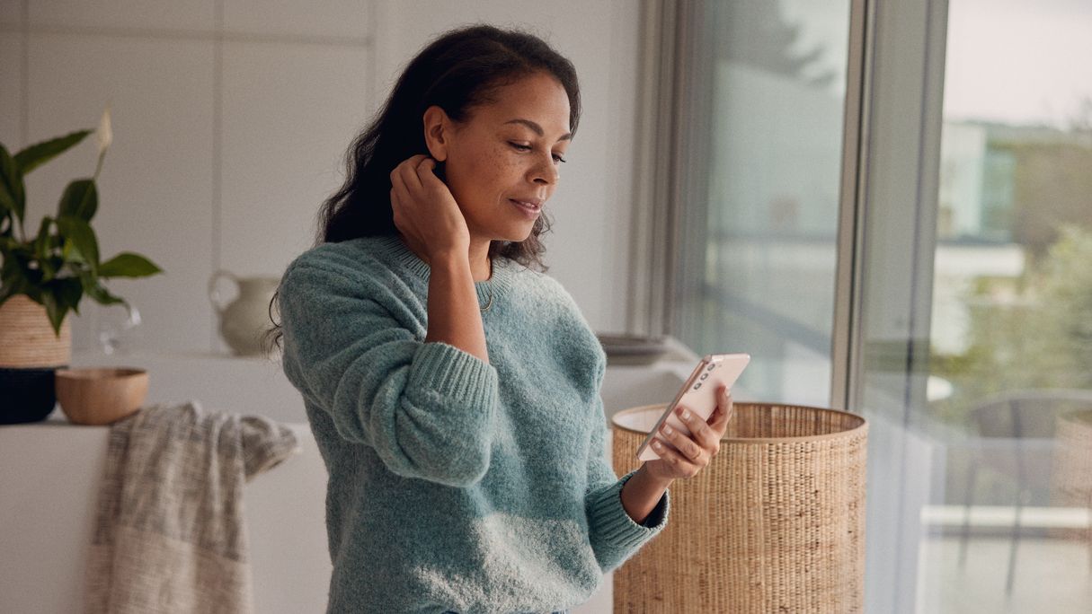 Eine Frau steht am Fenster und blickt auf ihr Smartphone