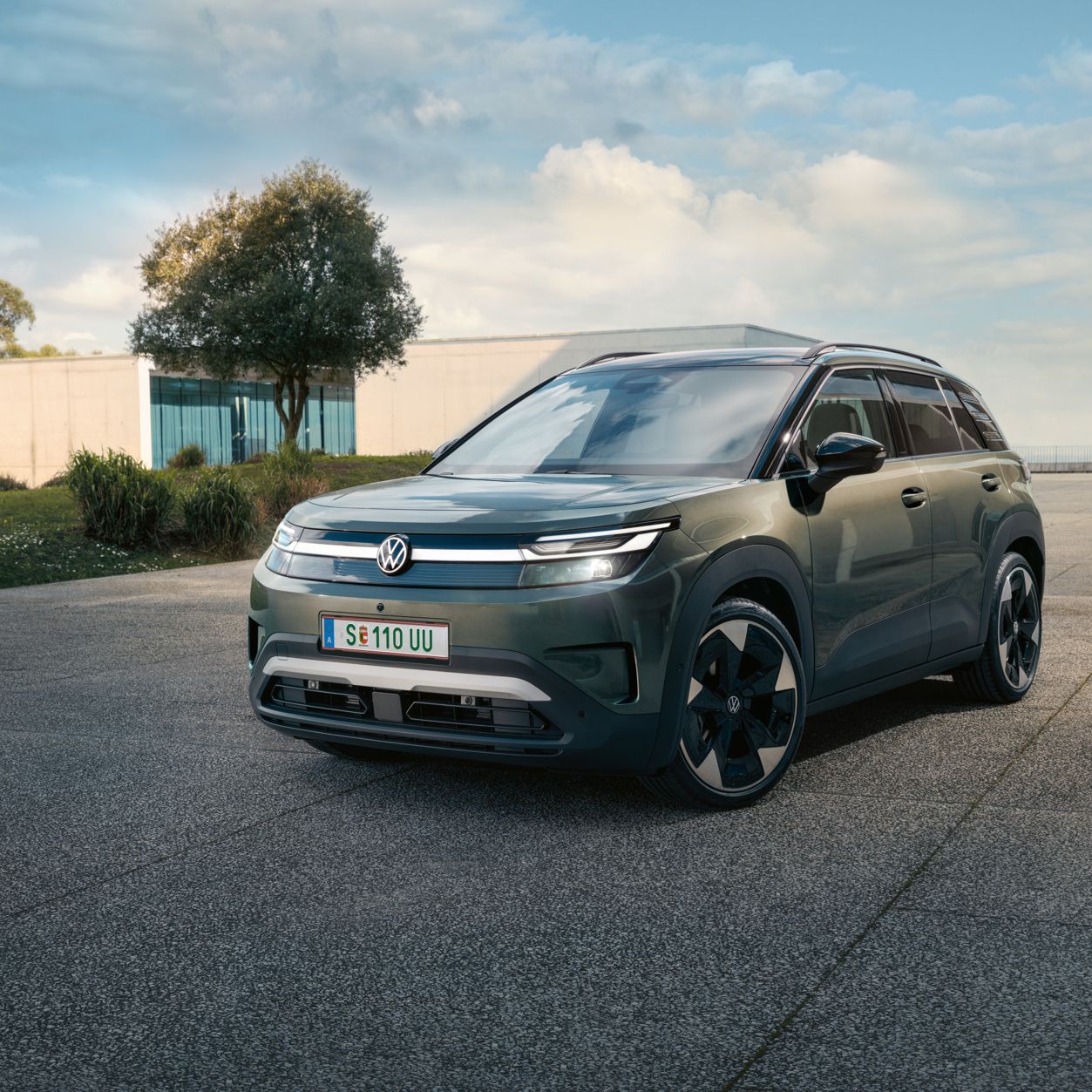 Ein grüner VW ID. Cross steht vor einem modernen Glasgebäude auf einer Betonfläche.