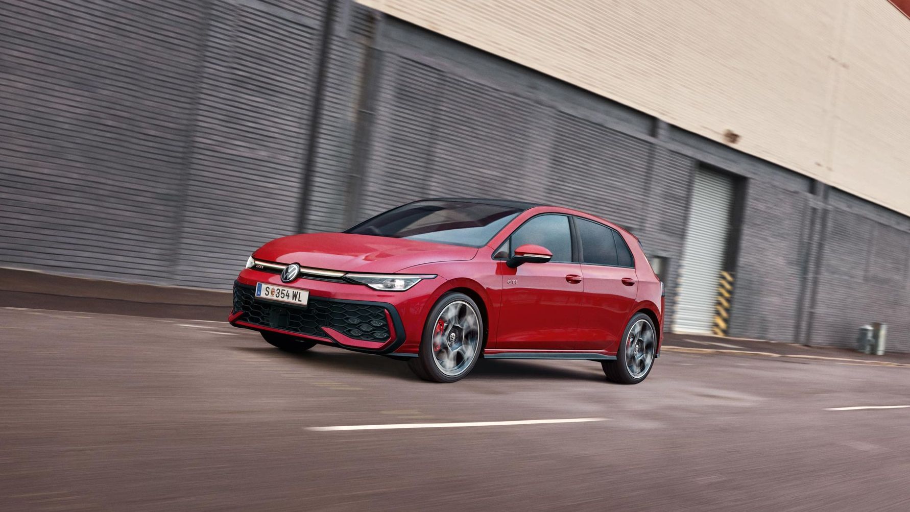 Ein roter VW Golf GTI fährt vor einer Lagerhalle entlang.