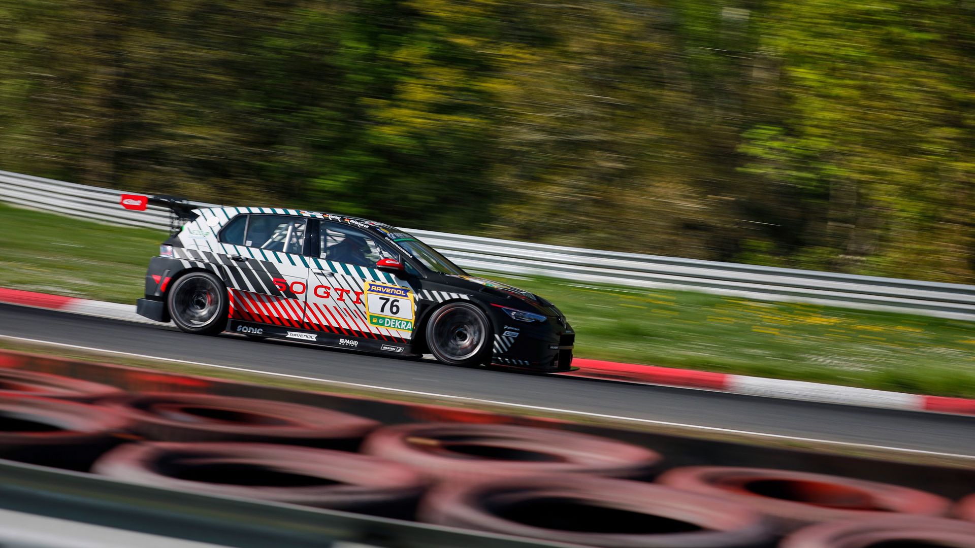 Ein Golf GTI Clubsport mit der Nummer 76 fährt schnell auf einer Rennstrecke. Der Hintergrund ist verschwommen, da der Wagen in Bewegung ist. Die Reifen am Streckenrand sind gut sichtbar.