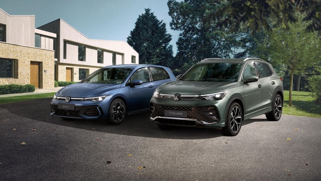 Zwei VW Modell, ein blauer Golf und ein grüner Tiguan, stehen nebeneinander auf einer Einfahrt vor einem Reihenhaus. Das Umfeld ist grün und bewaldet, das Wetter scheint klar zu sein.