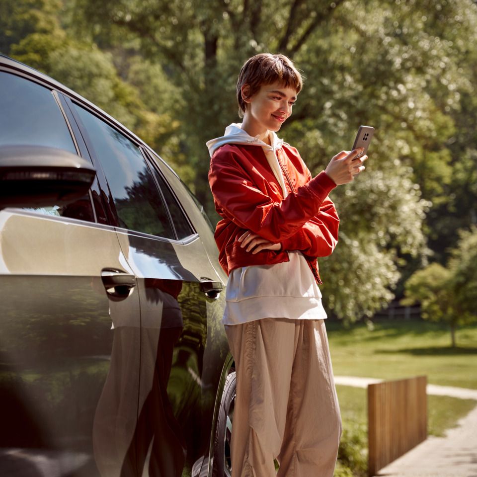 Eine Frau mit einem Smartphone steht neben ihrem ID.3