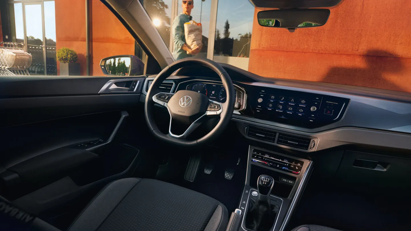Interieur des VW Polo mit Infotainmentsystem, Multifunktionslenkrad und Digital Cockpit. Ein Mann läuft vor dem Auto entlang.