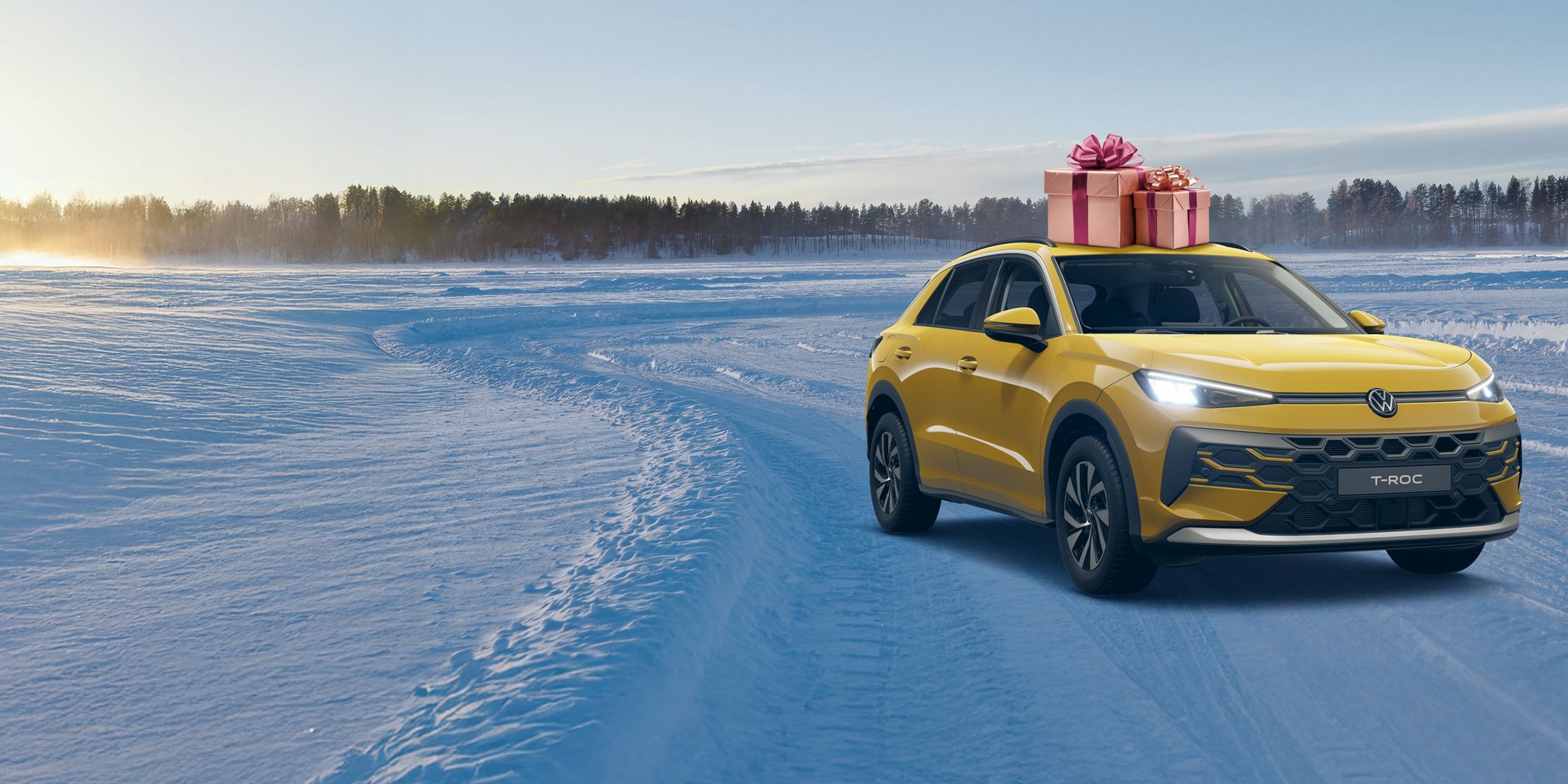 Ein gelbes Auto fährt durch eine verschneite Landschaft bei Sonnenaufgang. Auf dem Dach des Autos befindet sich eine große Geschenkbox mit einer roten Schleife. Im Hintergrund sind Bäume im Schnee zu sehen.