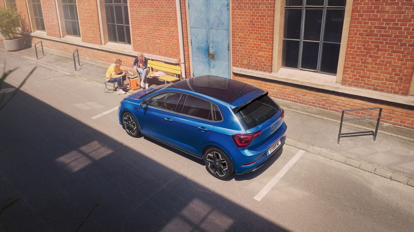 Blick von schräg oben auf einen parkenden VW Polo R-Line mit Roof-Pack, neben dem Auto spielt ein Pärchen Schach.