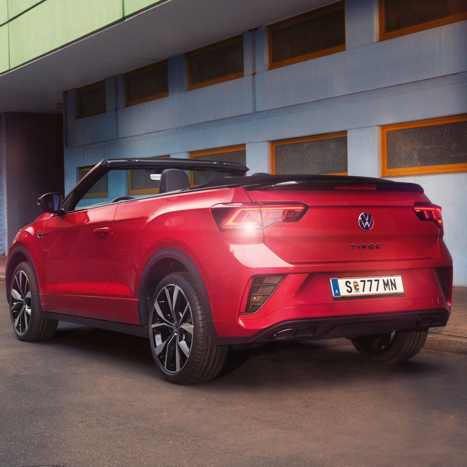 Ein rotes VW T-Roc Cabriolet mit geöffnetem Verdeck parkt am Straßenrand in Heckansicht.