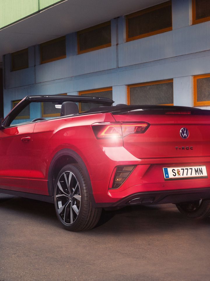 Ein rotes VW T-Roc Cabriolet mit geöffnetem Verdeck parkt am Straßenrand in Heckansicht.