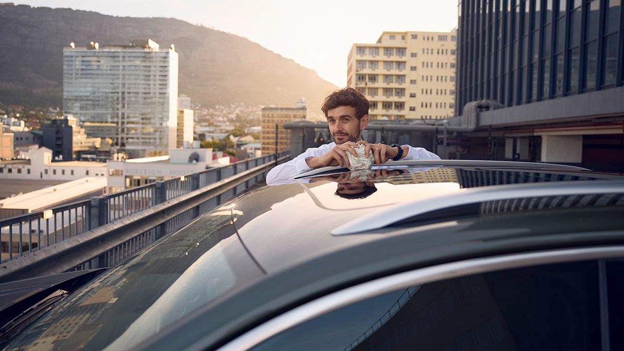 Ein Mann steht neben seinem Volkswagen T-Roc und blickt über eine Stadt.
