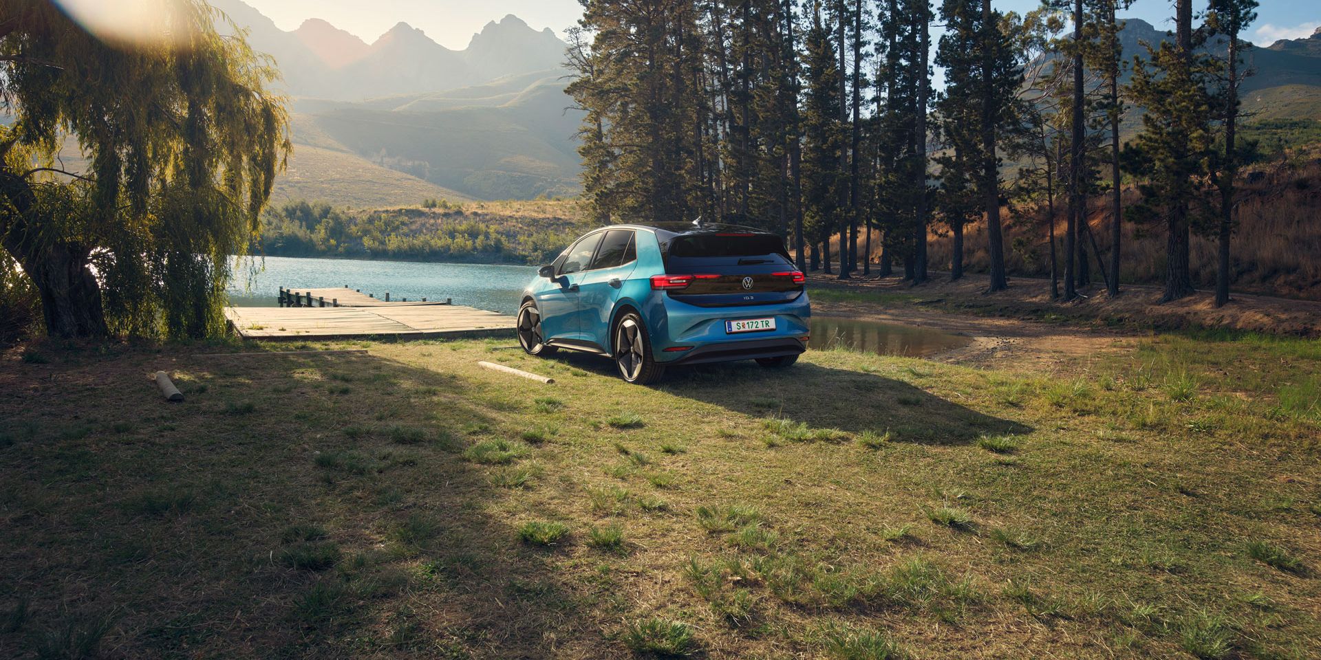 Ein blauer ID.3 steht am Ufer eines Sees, umgeben von hohen Bäumen.