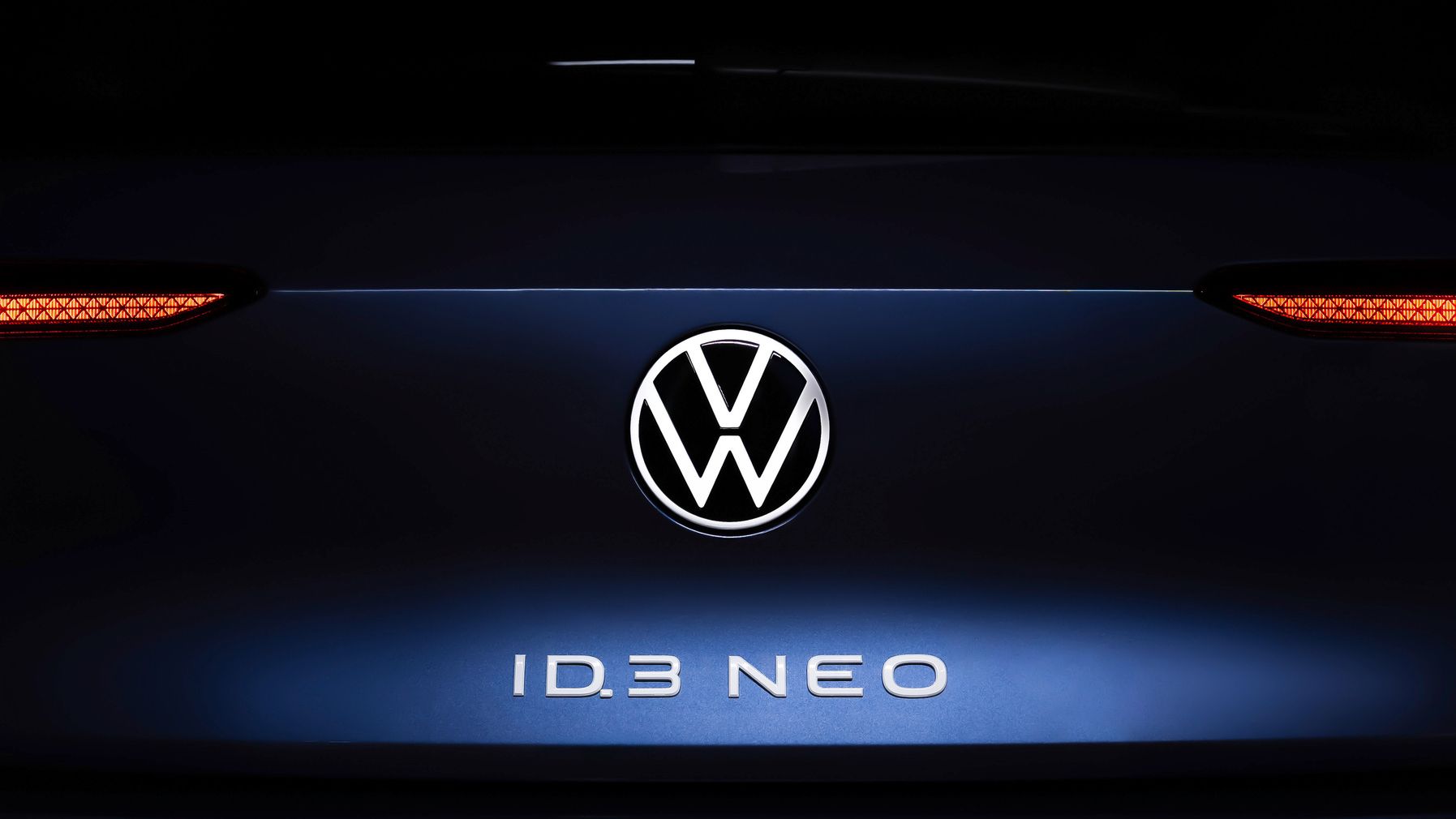 Nahaufnahme des Hecks eines Volkswagen ID.3 NEO. Im Zentrum ist das Volkswagen-Logo beleuchtet, darunter steht der Schriftzug "ID.3 NEO". Die Rücklichter sind auf beiden Seiten des Logos sichtbar.