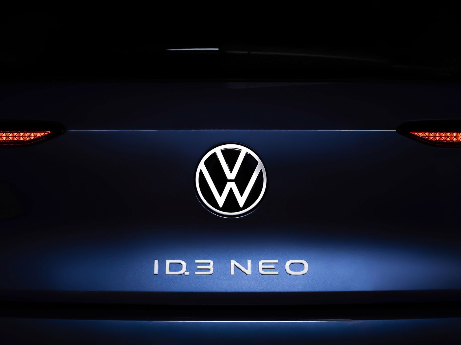 Nahaufnahme des Hecks eines Volkswagen ID.3 NEO. Im Zentrum ist das Volkswagen-Logo beleuchtet, darunter steht der Schriftzug "ID.3 NEO". Die Rücklichter sind auf beiden Seiten des Logos sichtbar.