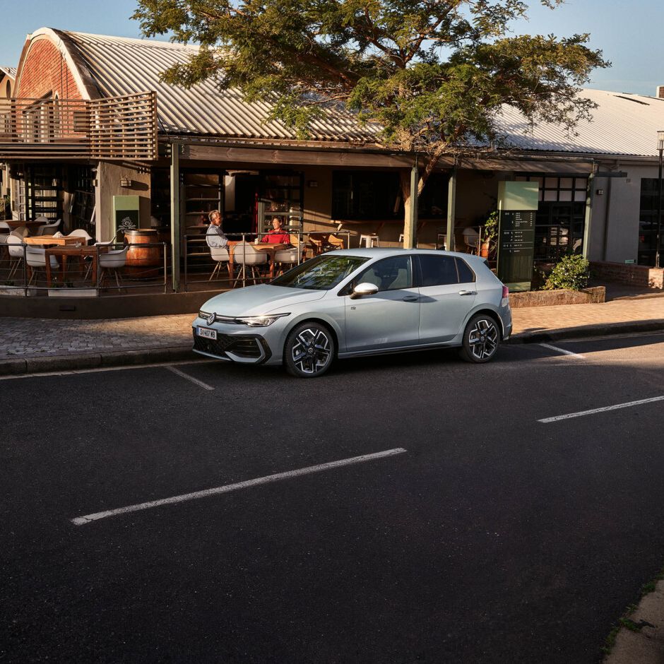 Seitenansicht eines grauen VW Golf, der vor einem Lokal parkt.