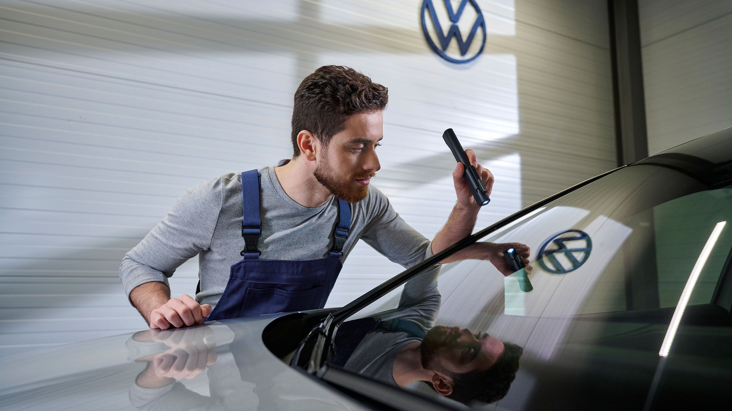 Ein Volkswagen Techniker kontrolliert mit einer Taschenlampe die Windschutzscheibe eines Volkswagen.