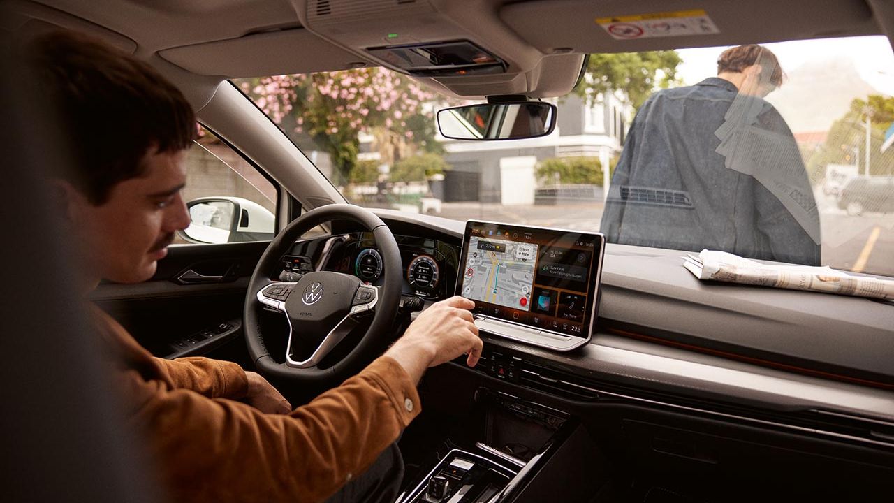 Ein Mann sitzt im parkenden VW Golf und bedient das Navigationssystem.