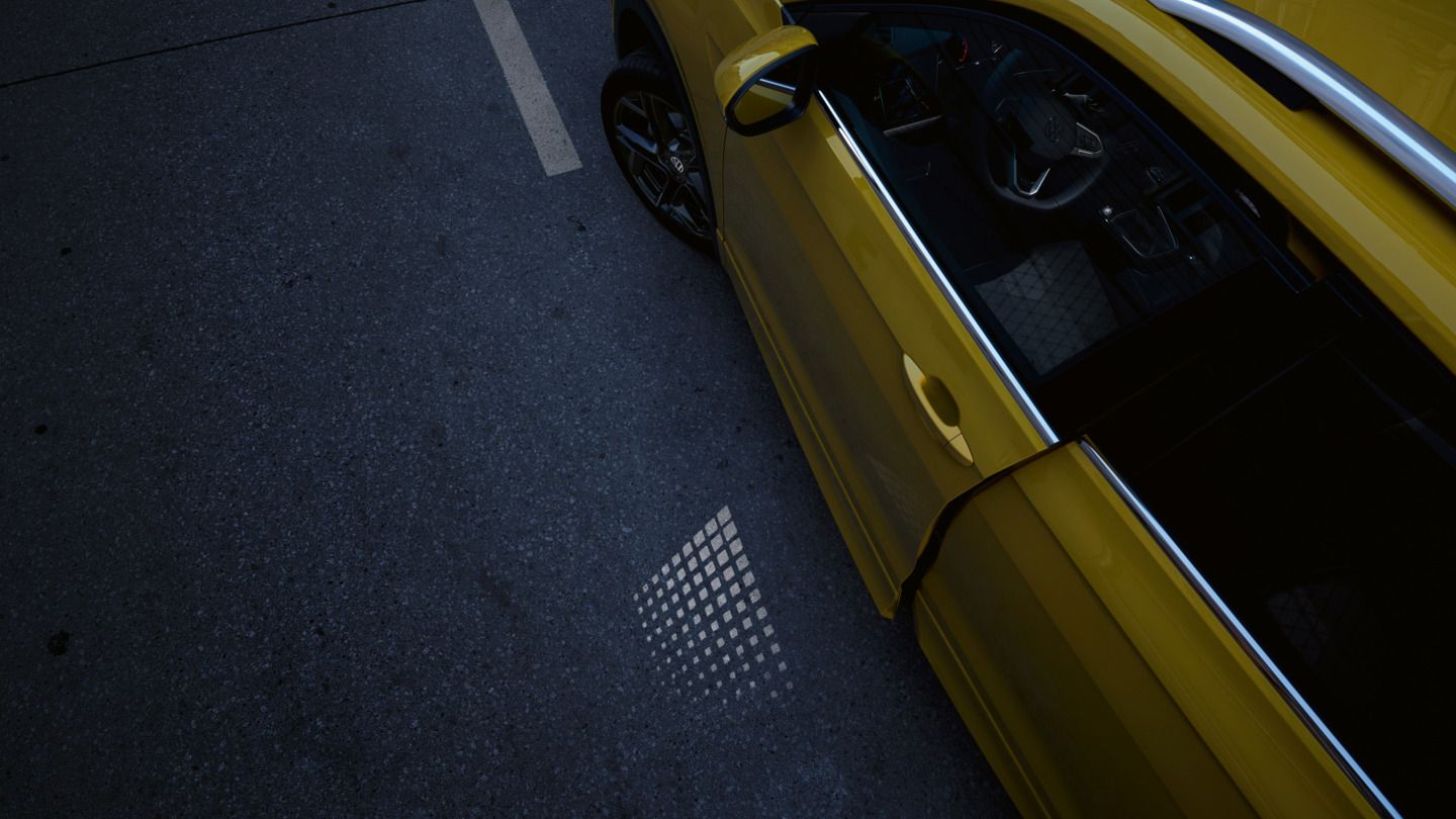 Die nur einen Spalt geöffnete VW T-Cross Fahrertür von oben, mit sichtbarer Lichtprojektion in der Dämmerung.