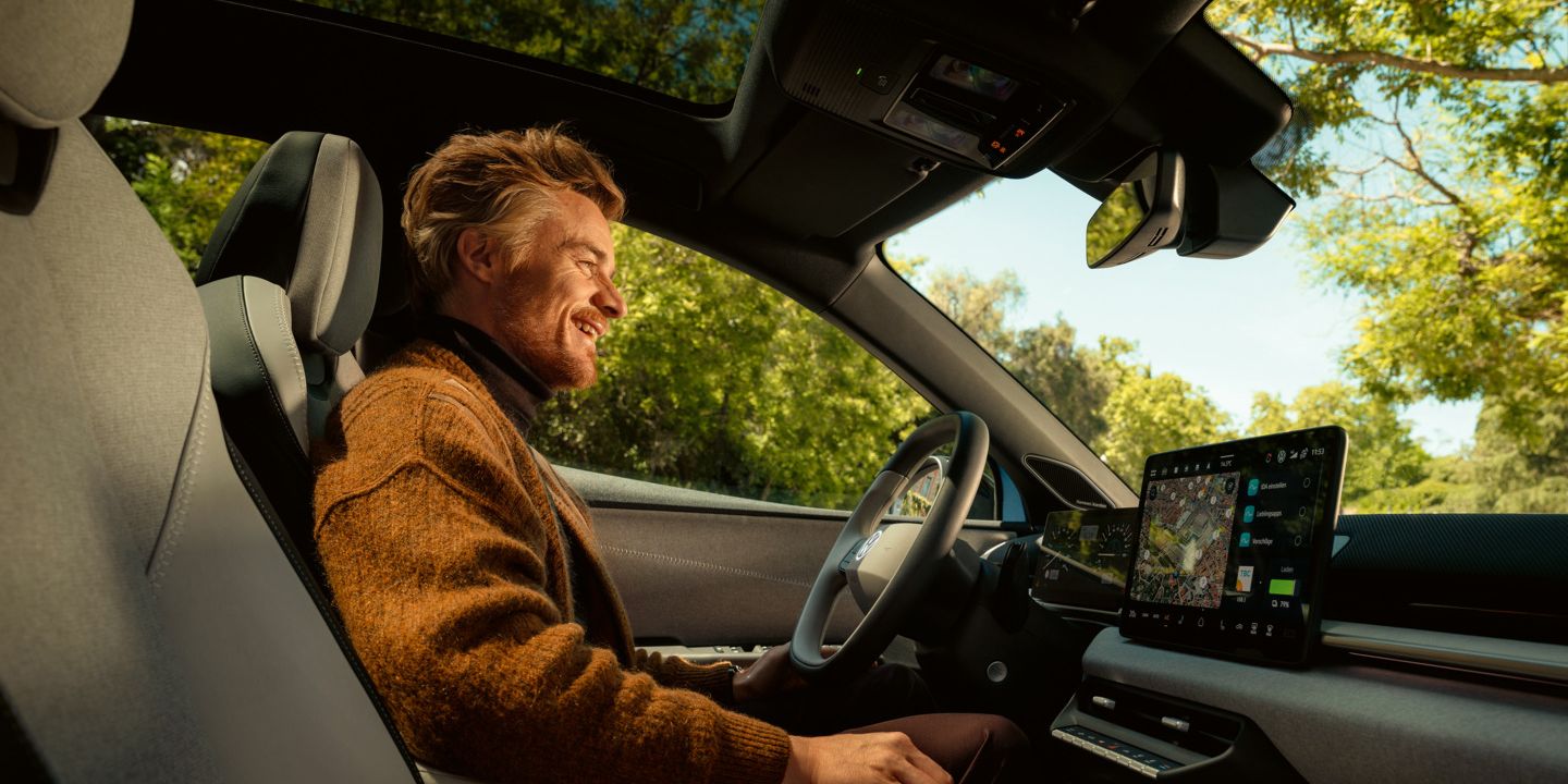 Ein Mann sitzt auf dem Fahrersitz eines VW ID. Polo, das Panoramadach und das Infotainment sind zu sehen.