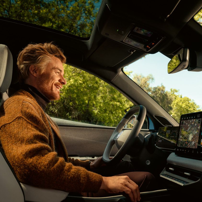 Ein Mann sitzt auf dem Fahrersitz eines VW ID. Polo, das Panoramadach und das Infotainment sind zu sehen.