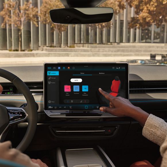 Zwei Frauen sitzen im ID.7 und bedienen die Sitzheizung über das Touchdisplay des Infotainmentsystems