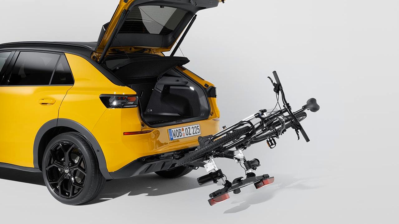 Ein Volkswagen Fahrradheckträger mit Fahrrad, abgeklappt am Heck eines gelben Volkswagen T-Roc mit geöffnetem Kofferraum.