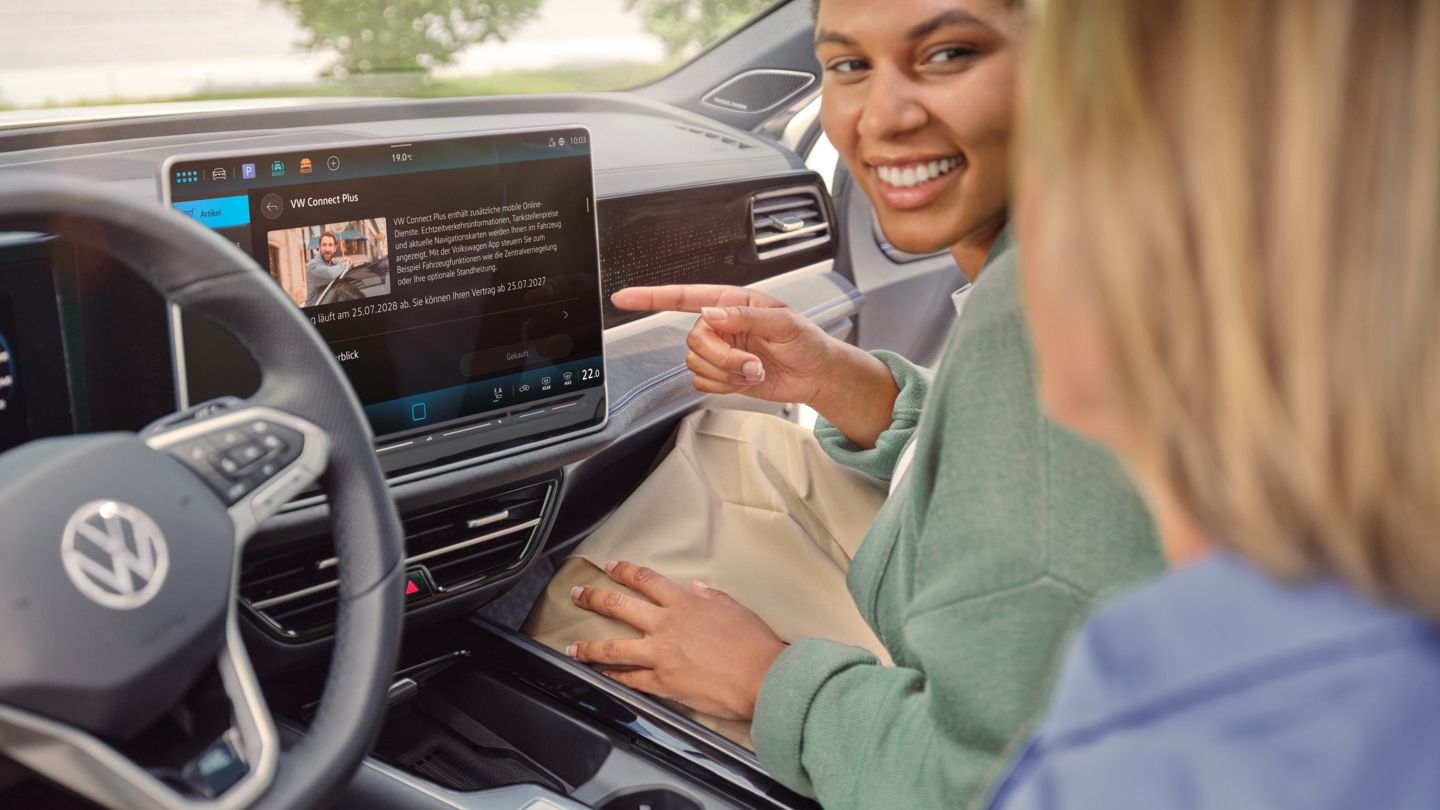 Eine Frau sitzt am Beifahrersitz des VW Passat und zeigt auf das Infotainmentsystem