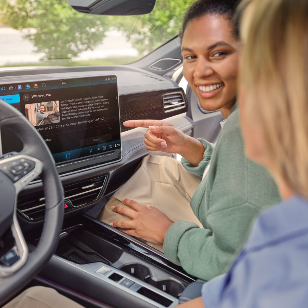 Eine Frau sitzt am Beifahrersitz des VW Passat und zeigt auf das Infotainmentsystem