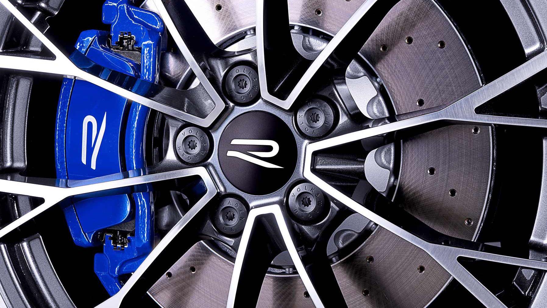 Nahaufnahme eines Autobremsrads mit blauem Bremssattel. Die silberne Felge mit markantem R-Logo steht im Vordergrund.