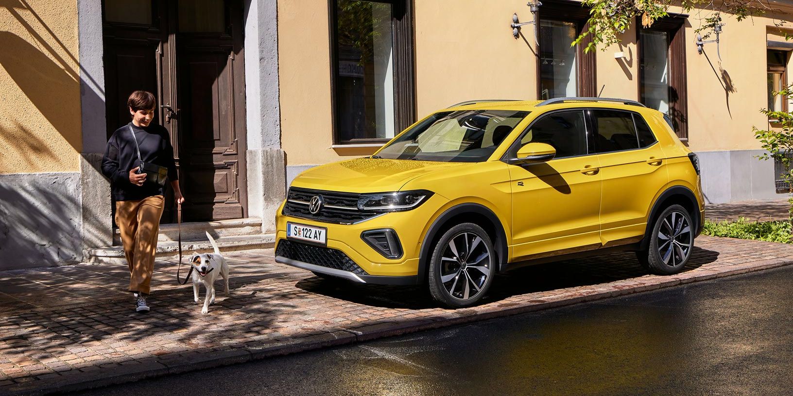 VW T-Cross parkt am Straßenrand, Frau mit kleinem Hund geht an ihm vorbei