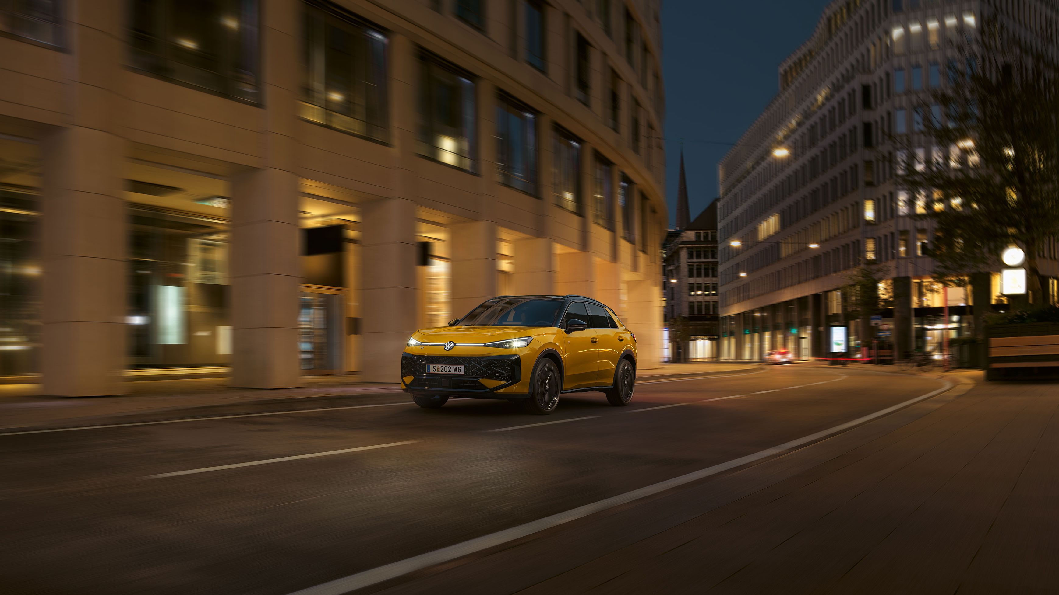 Ein gelber VW T-Roc R-Line fährt nachts durch eine urbane Umgebung.