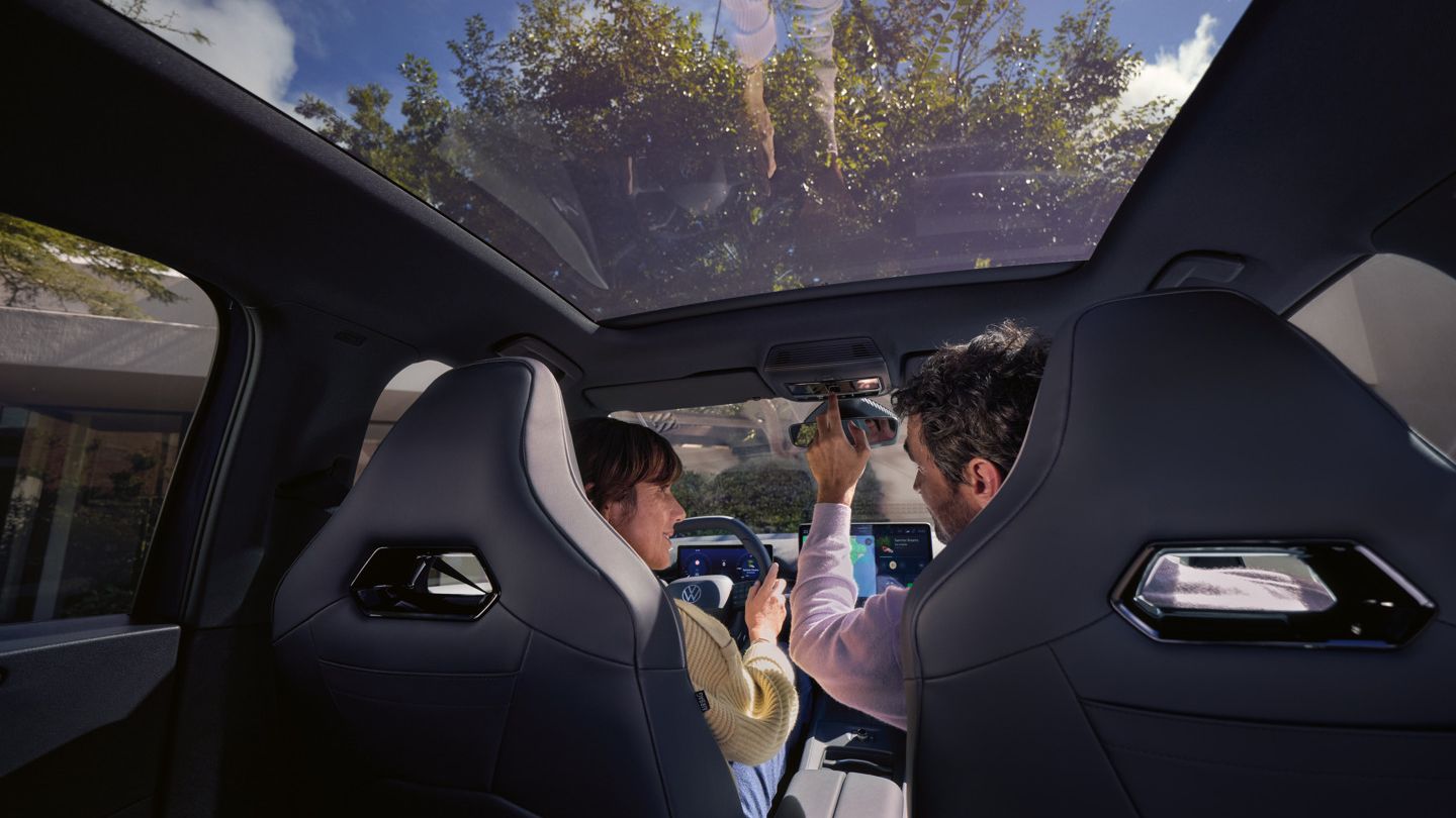 Eine Frau und ein Mann sitzen in einem VW ID.3 Neo, der Mann bedient das Panoramadach