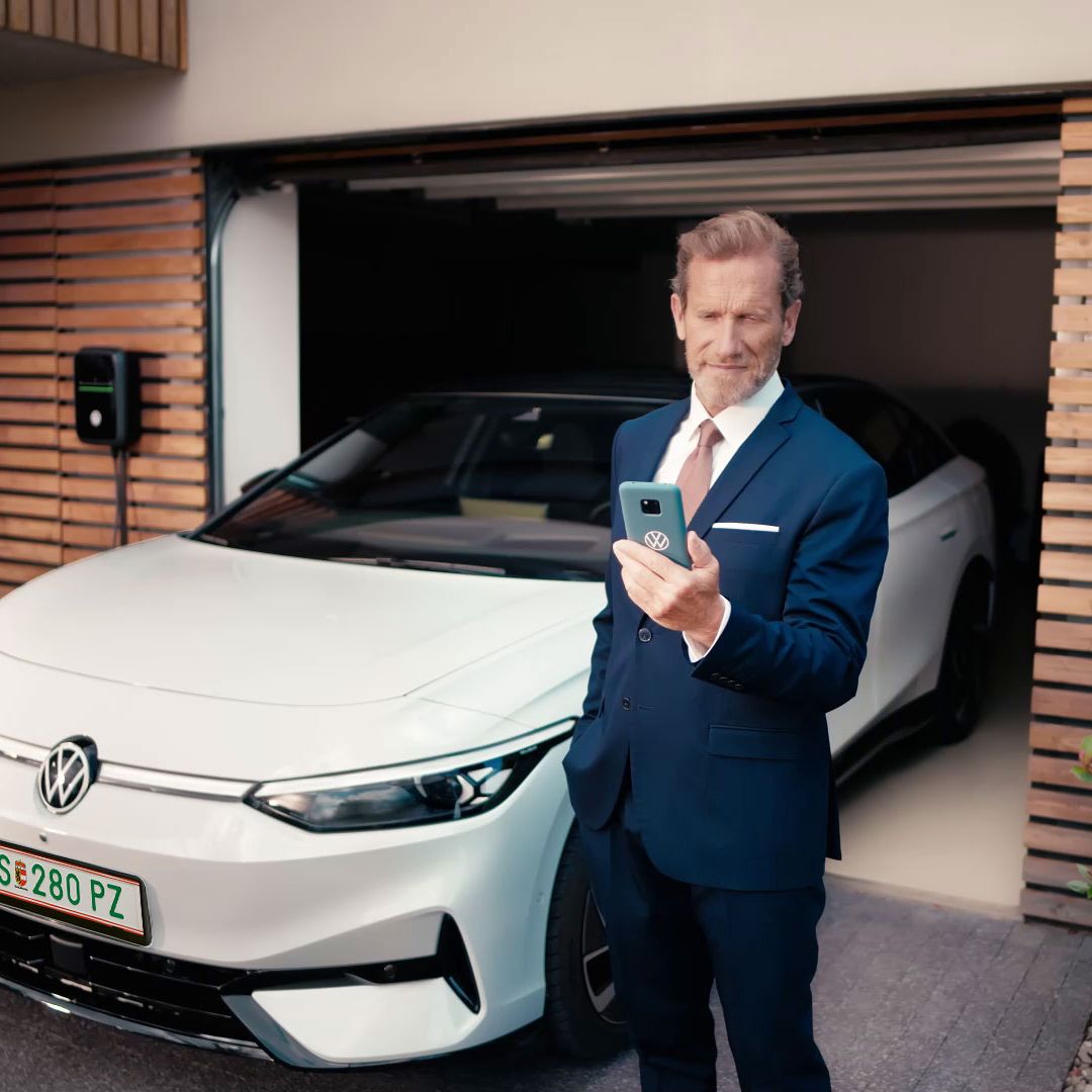 Geschäftsmann schaut auf sein Handy vor seinem in der Garage geparkten ID.7