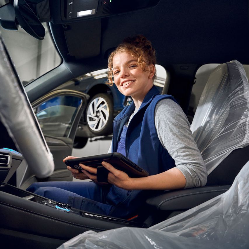 Eine Volkswagen Technikerin sitzt mit ihrem Tablet in einem Volkswagen Tiguan