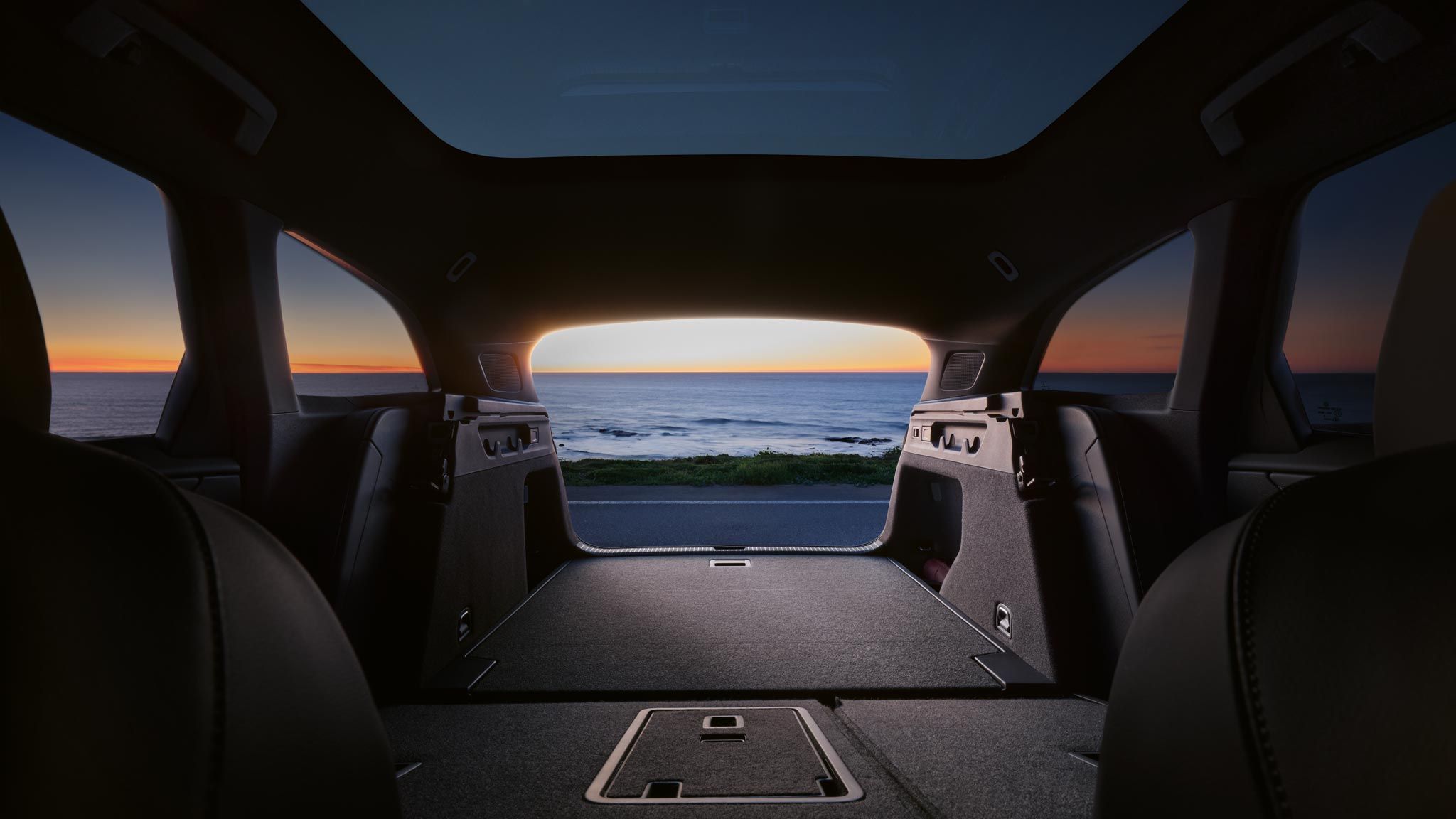 Innenansicht des Kofferraums eines VW ID.7 Tourer mit umgeklappten Rücksitzen, durch die offene Heckklappe ist das Meer sichtbar.