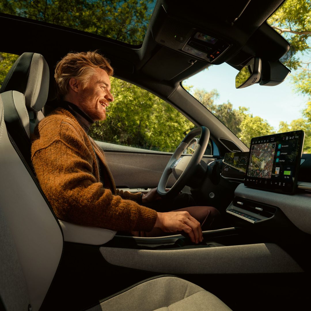 Ein Mann sitzt auf dem Fahrersitz eines VW ID. Polo, das Panoramadach und das Infotainment sind zu sehen.