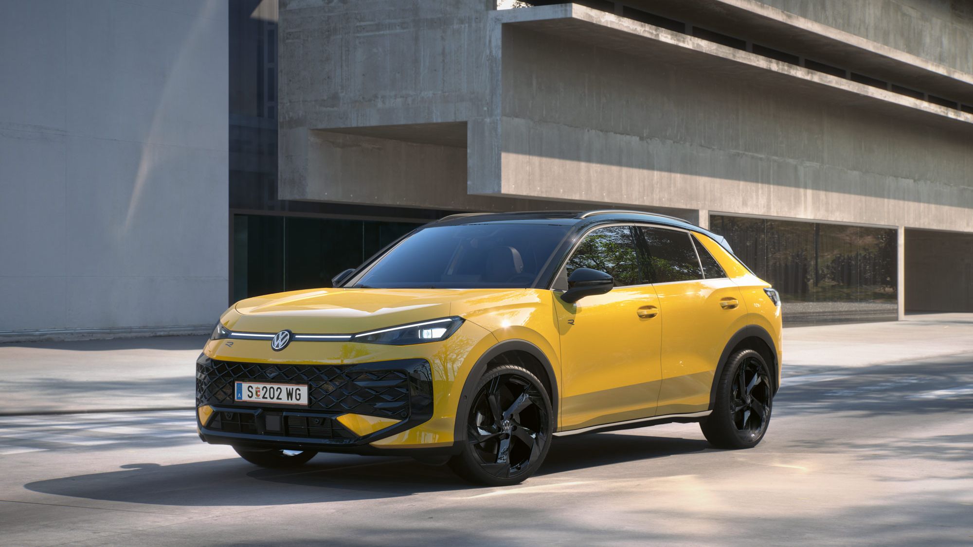Eine gelber Volkswagen T-Roc R-Line steht in 3/4-Frontansicht vor einem Gebäude.