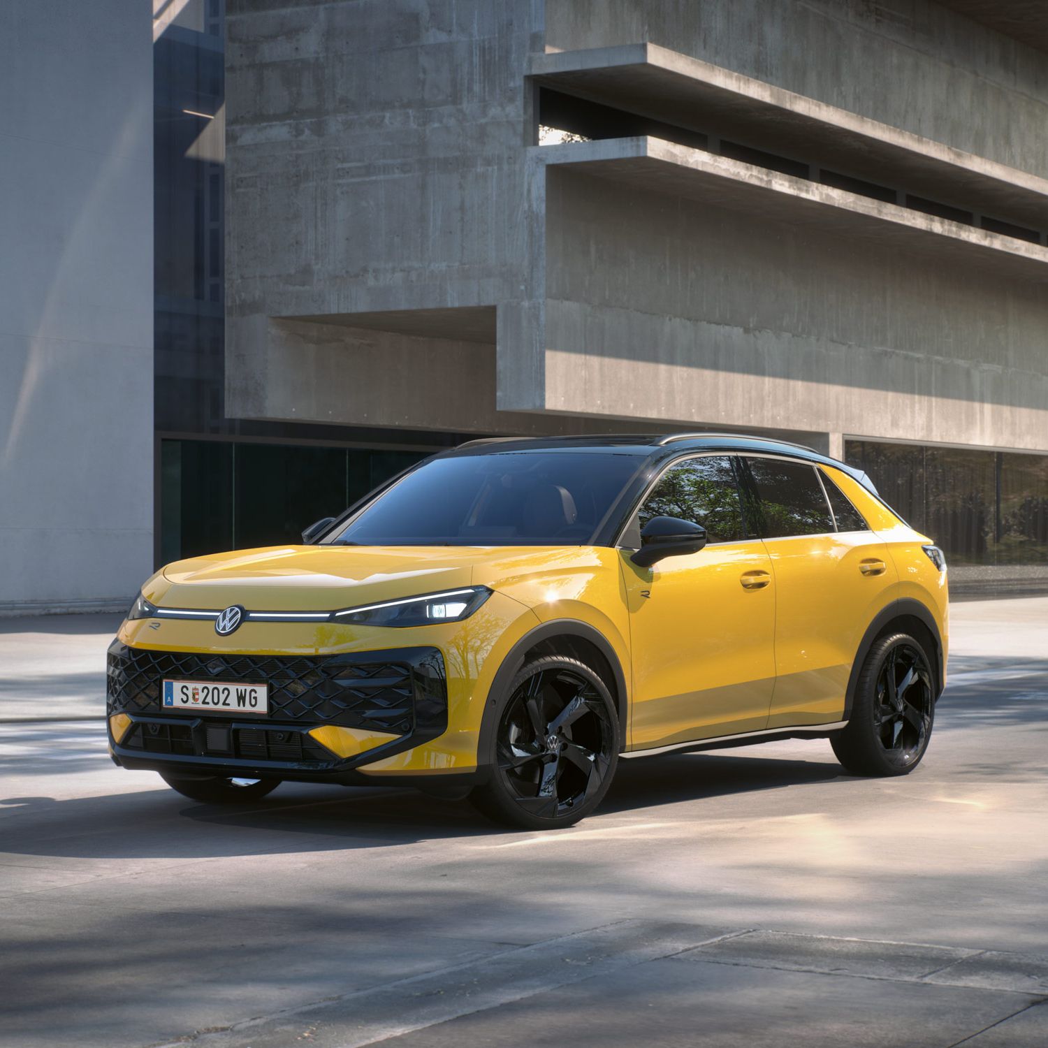 Eine gelber Volkswagen T-Roc R-Line steht in 3/4-Frontansicht vor einem Gebäude.
