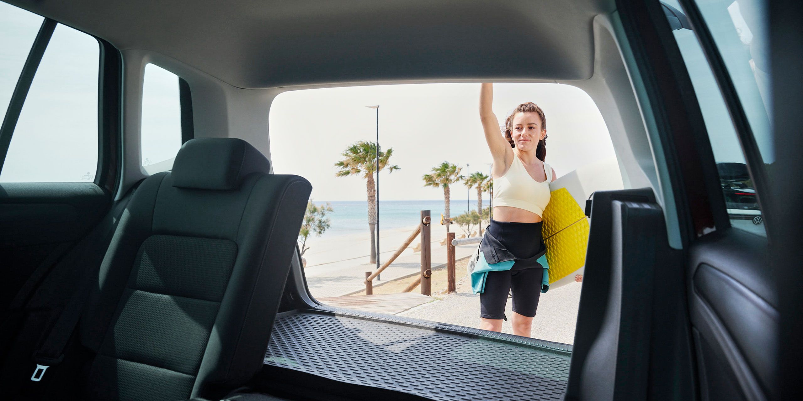 Blick durch das Heck eines Volkswagen Golf Sportsvan. Eine Frau schließt die Heckklappe.
