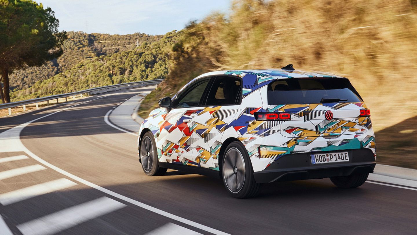 Ein ID. Polo mit bunter Lackierung fährt auf einer kurvenreichen Straße durch eine hügelige Landschaft. Auf der rechten Straßenseite sind Bäume und Büsche zu sehen. Der Himmel ist klar.