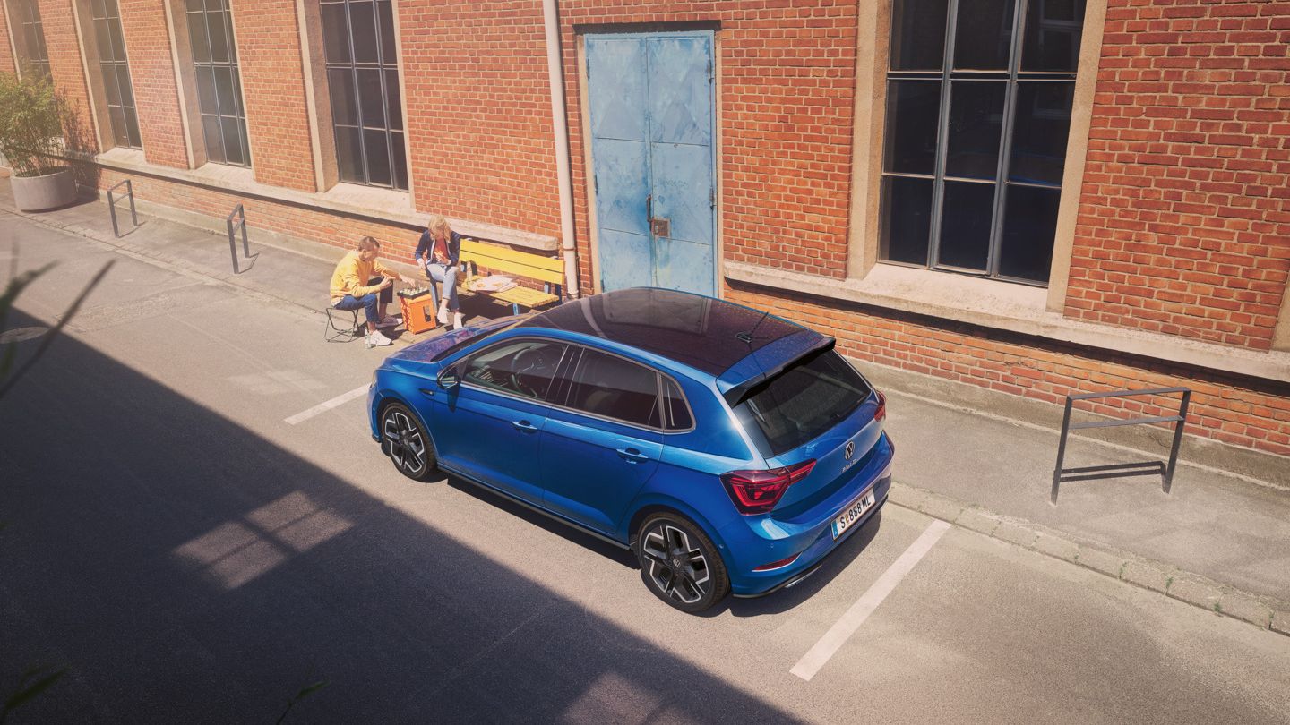 Blick von schräg oben auf einen parkenden VW Polo R-Line mit Roof-Pack, neben dem Auto spielt ein Pärchen Schach.