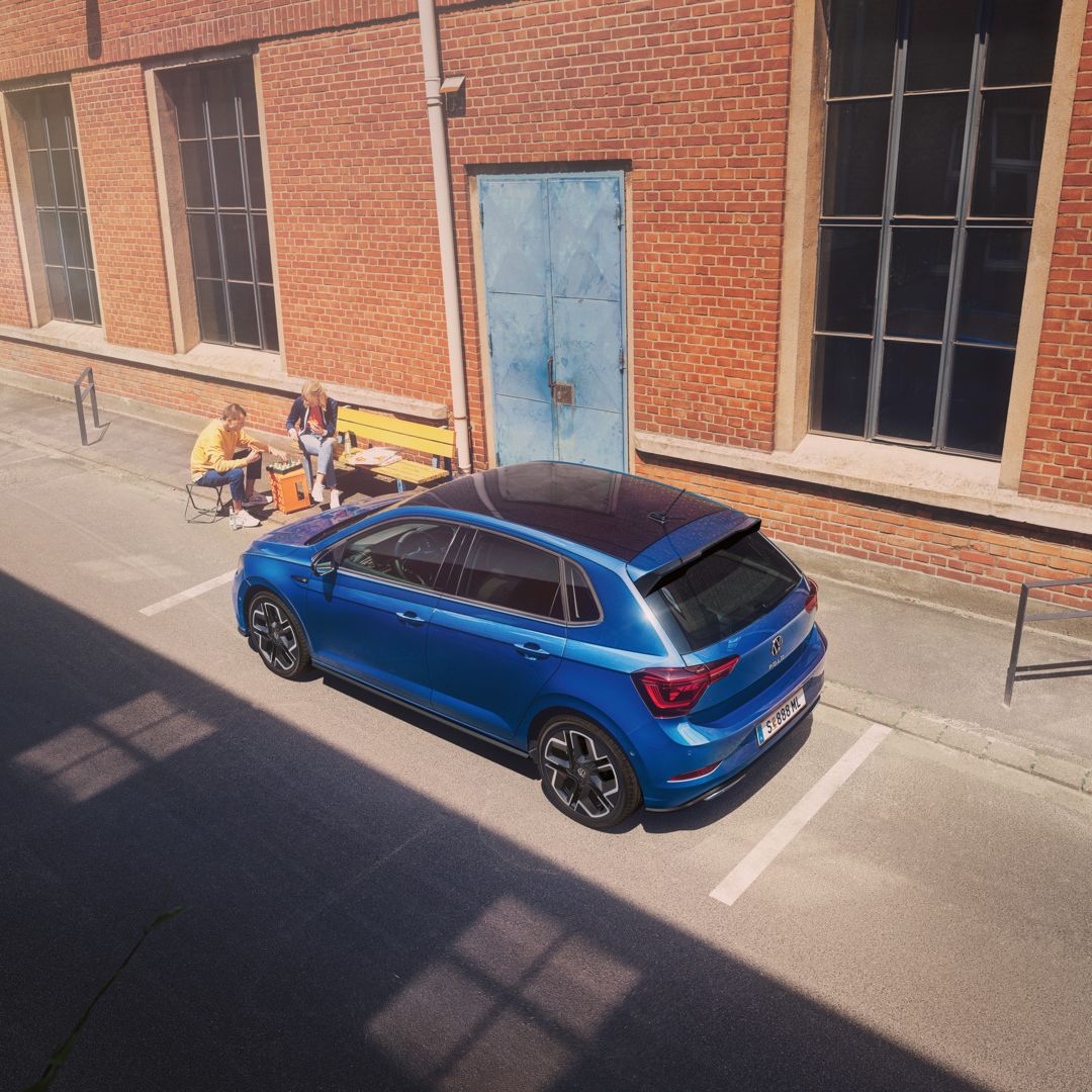 Blick von schräg oben auf einen parkenden VW Polo R-Line mit Roof-Pack, neben dem Auto spielt ein Pärchen Schach.