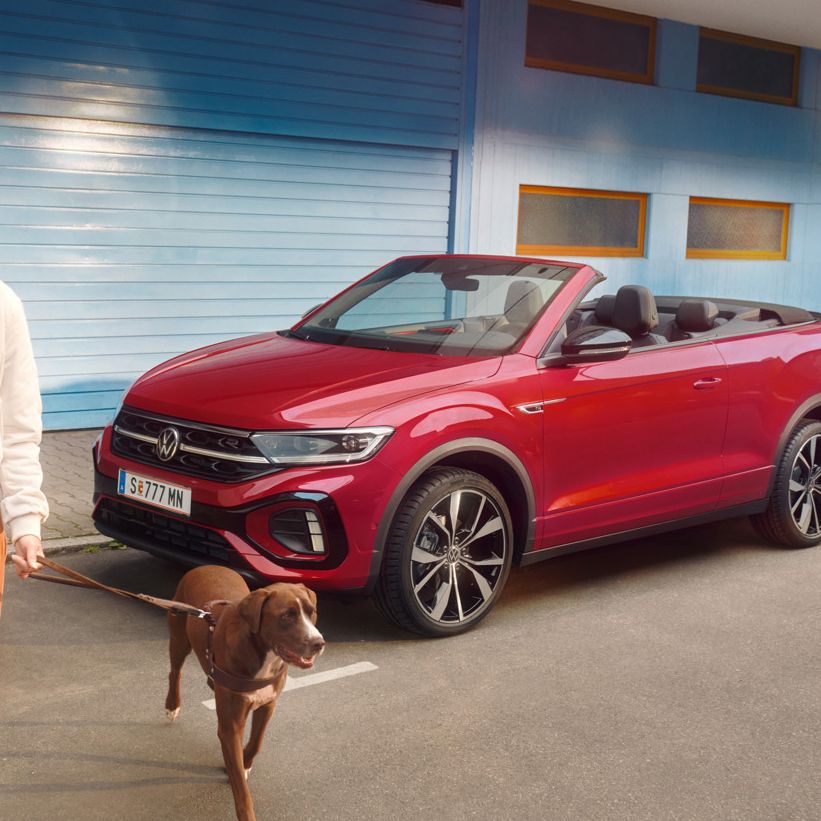 Frau geht mit zwei Hunden and der Leinen von einem roten VW T-Roc Cabrio weg