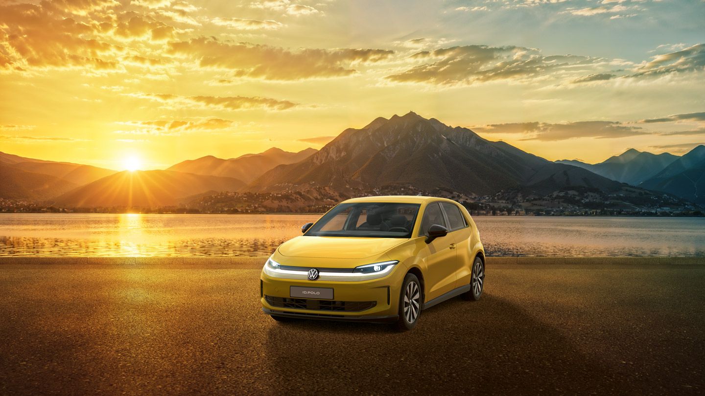 Gelber VW ID. Polo steht auf einer glatten Fläche vor einem See bei Sonnenuntergang. Im Hintergrund erheben sich dunkle Berge unter einem dramatisch goldenen Himmel mit verstreuten Wolken. Die Szene wirkt ruhig und betont das Auto als zentrales Motiv.