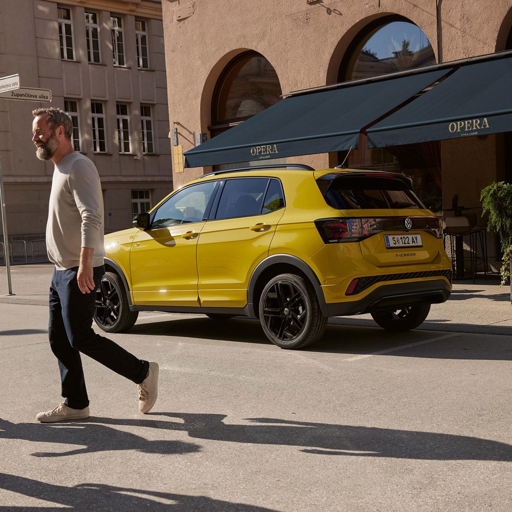 Ein gelber VW T-Cross ist in einer Stadt geparkt, eine Familie geht an ihm vorbei. 